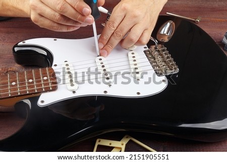 Guitar technician adjusts the height pickups on black electric guitar.