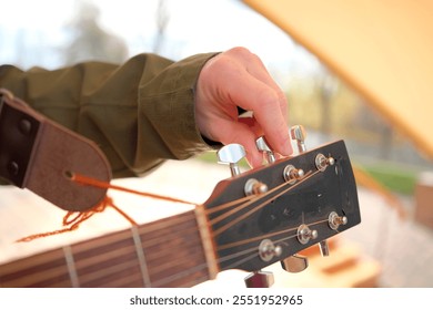 The guitarist holds the guitar and adjusts the pegs. The concept of focus and dedication to improving the instrument. Adjusting the tones and frets of the guitar, focus on the hand, close-up - Powered by Shutterstock