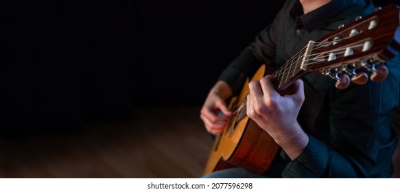 Guitarist male hands playing the guitar. Classical concert, performance rehearsal, show. Banner with copy space. The guy in the dark shirt is plucking the strings of a six-string guitar