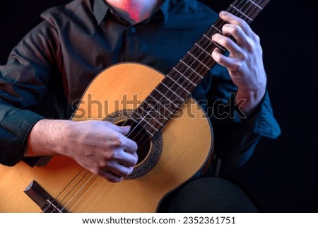 Guitarist male hands playing the guitar. Classical concert, performance rehearsal, show. Learning to play a musical instrument. The guy in the dark shirt is plucking the strings of a six-string guitar