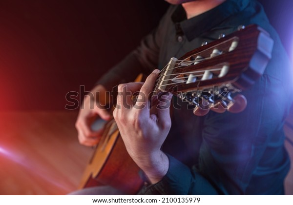 Guitarist male hands playing the guitar. Classical\
concert, performance rehearsal, show. Learning to play a musical\
instrument. The guy in the dark shirt is plucking the strings of a\
six-string guitar