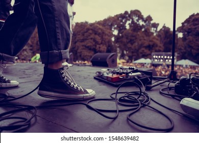 Guitarist perfroming live on hardrock concert stage outdoor.Feet of bass guitar player playing solo part on rock festival in summer.Punk band perform on scene,focus on old dirty sneakers of musician