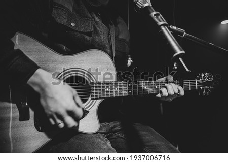 The guitarist plays an acoustic guitar with a capo in front of a microphone. The concept of music recording, rehearsal or live performance.