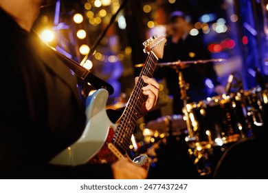 A guitarist plays a chord on the fretboard during a band's performance. Close-up, soft lights on the background - Powered by Shutterstock