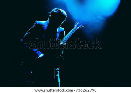 Guitarist silhouette in a dark on a stage in blue lights playing solo