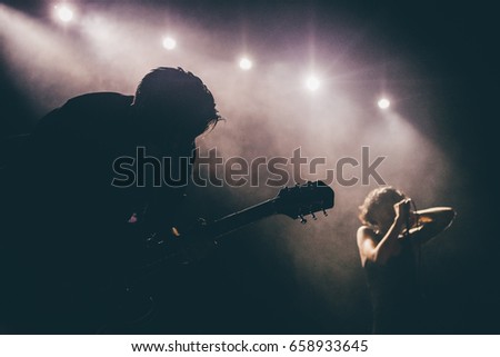Guitarist silhouette on a stage in a backlights in the smoke playing solo with the female singer at background