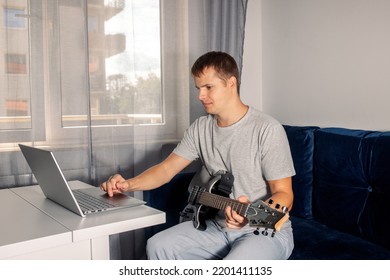 Guitarist Is Watching A Virtual Video Tutorial At Home. Hobby. Man Learn To Play Guitar Online. The Guy Is Sitting At Home On The Divan And Watching An Online Lesson, Learning To Play The Guitar.