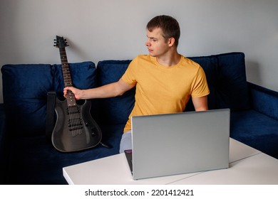 Guitarist Is Watching A Virtual Video Tutorial At Home. Hobby. Man Learn To Play Guitar Online.  The Guy Is Sitting At Home On The Sofa And Watching An Online Lesson, Learning To Play The Guitar.