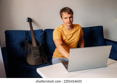 Guitarist Is Watching A Virtual Video Tutorial At Home. Hobby. Man Learn To Play Guitar Online.  The Guy Is Sitting At Home On The Sofa And Watching An Online Lesson, Learning To Play The Guitar.