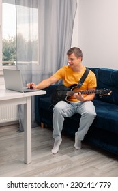 Guitarist Is Watching A Virtual Video Tutorial At Home. Hobby. Man Learn To Play Guitar Online.  The Guy Is Sitting At Home On The Sofa And Watching An Online Lesson, Learning To Play The Guitar.