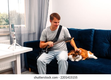 Guitarist Is Watching A Virtual Video Tutorial At Home. Hobby. Man Learn To Play Guitar Online.  The Guy Is Sitting At Home On The Sofa And Watching An Online Lesson, Learning To Play The Guitar.