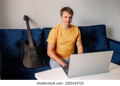 Guitarist Is Watching A Virtual Video Tutorial At Home. Hobby. Man Learn To Play Guitar Online.  The Guy Is Sitting At Home On The Sofa And Watching An Online Lesson, Learning To Play The Guitar.