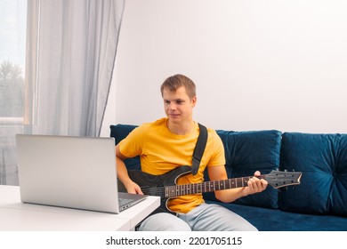 Guitarist Is Watching A Virtual Video Tutorial At Home. Hobby. Man Learn To Play Guitar Online.  The Guy Is Sitting At Home On The Sofa And Watching An Online Lesson, Learning To Play The Guitar.