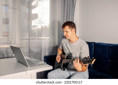 Guitarist Is Watching A Virtual Video Tutorial At Home. Hobby. Man Learn To Play Guitar Online.  The Guy Is Sitting At Home On The Sofa And Watching An Online Lesson, Learning To Play The Guitar.