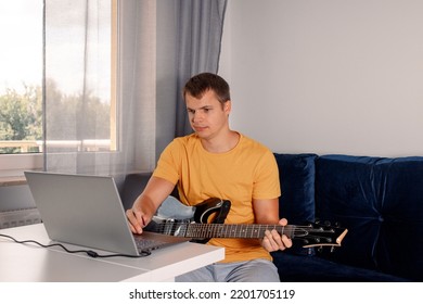 Guitarist Is Watching A Virtual Video Tutorial At Home. Hobby. Man Learn To Play Guitar Online.  The Guy Is Sitting At Home On The Sofa And Watching An Online Lesson, Learning To Play The Guitar.