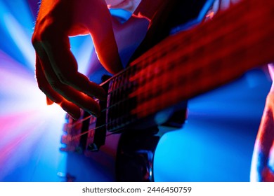 Guitarist's hands plucking strings of bass, electric guitar with dynamic stage lighting on blurred background. Concept of rock and classic music, hobby and work, energy, music festivals, concerts. Ad - Powered by Shutterstock