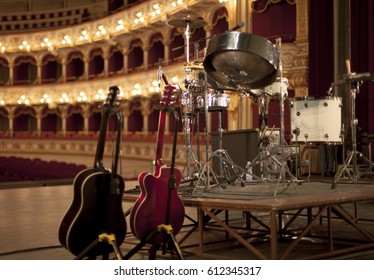 Guitars And Drumkits On A Stage In A Classic Theater, Ready For The Coming Rock Music Show. Shot From Behind.
