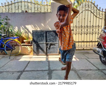 Gulbarga,India- February 15th 2021; Stock photo of Indian kid wearing orange color t shirt and short playing cricket in front yard of the house during his holidays.Picture captured under bright light.