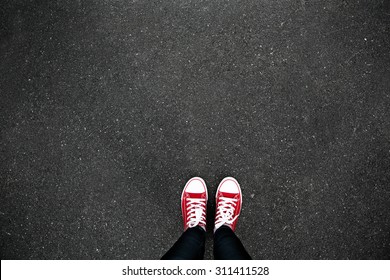 Gumshoes On Urban Grunge Background Of Asphalt. Conceptual Image Of Legs In Boots On City Street. Feet Shoes Walking In Outdoor. Youth Selphie Modern Hipster 