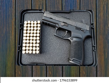 Gun And Bullet In The Case Box On Wooden Table