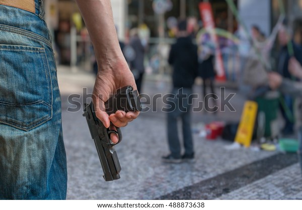 Gun control concept.\
Armed man - attacker holds pistol in hand in public place. Many\
people on street.