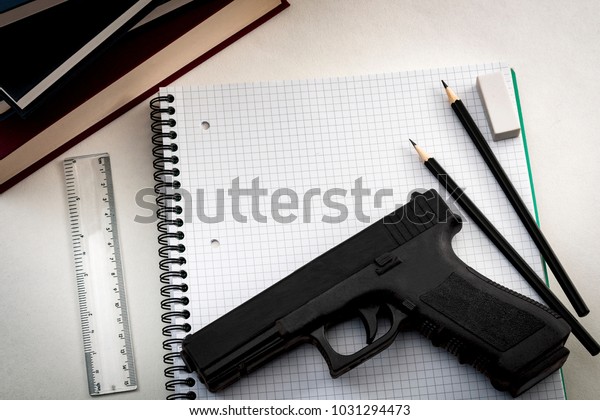 Gun control legislation and school shooting\
prevention concept with a gun on a notebook surrounded by school\
supplies and copy space
