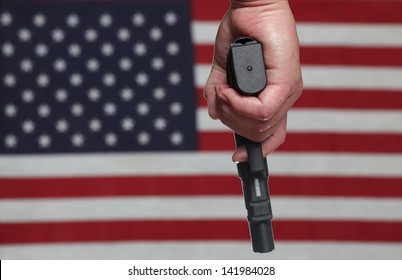 Gun Control USA Style/Hand Holding Automatic Pistol Over Slightly Blurred Background Of US Flag