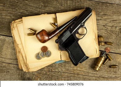 Gun and old book. Detective novel. Wooden tobacco pipe. Pistols and cartridges on the table