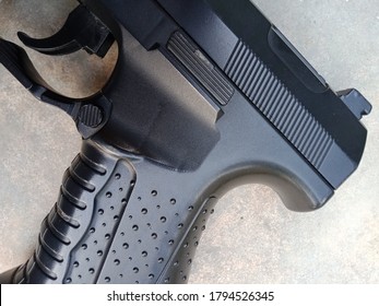 Gun On Floor. Black Handgun On The Cemented Floor. Closeup Of Grip And Trigger Of Handgun Showing Texture Of Gun Metal.