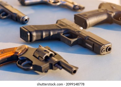 A gun on the table among the weapons, selective focus. Crime news background. The concept of rules for the owners of firearms. Shooting training. Confiscation of contraband and illegal carrying.