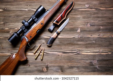 A Gun With An Optical Sight, A Hunting Knife On A Wooden Background.Top View.