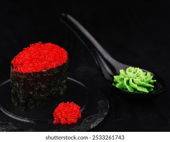 Gunkan maki sushi with tobiko flying fish roe is presented on a black slate plate with wasabi and a pink flower - Powered by Shutterstock