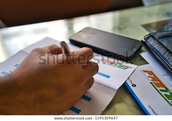 Gurgaon - India, Circa 2019: Photograph of Fast Tag\
application form being filled with a fountain pen, along with a\
wallet and a mobile phone on a beautifully decorated table. Fast\
tag is expected to