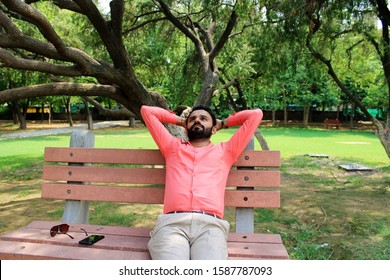 Gurgaon/Gurugram, Haryana, India - 21 July,2019: Young Bearded Man Sitting Daydreaming On A Cemented Park Bench With His Hands Clasped Behind His Head.