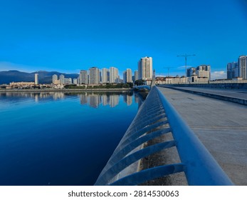 Gurney Bridge, an important link between Gurney Drive, and the small town in the Andaman Islands. City skyline reflects in calm waters below. Modern buildings stretch behind gentle clouds. Walking path invites quiet strolls beside metal railings.