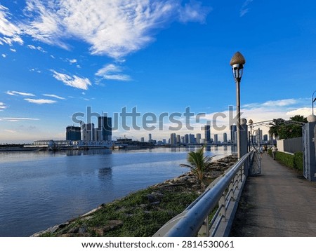 Gurney Bridge, an important link between Gurney Drive, and the small town in the Andaman Islands. City skyline reflects in calm waters below. Modern buildings stretch behind gentle clouds. Walking path invites quiet strolls beside metal railings.