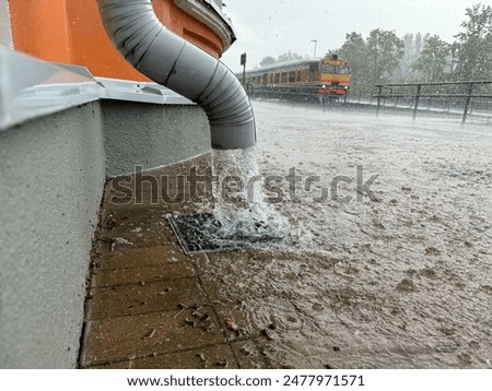 Gutter  by the wall of the building and train in the background, rapid flow of water after heavy rain.
