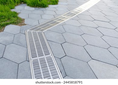 A gutter, a drain for rainwater on the border of a lawn and a pedestrian path in the park. The connection of the grids, the rotation of the drainage system. Selective focus. - Powered by Shutterstock