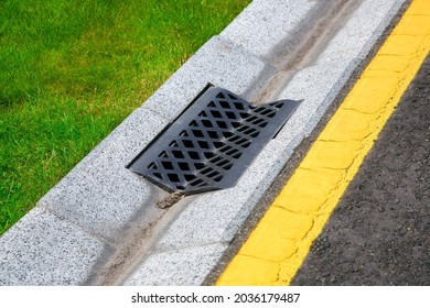 Gutter Of A Stormwater Drainage System On The Side Of An Road With Yellow Markings And Green Lawn On Dry Weather.