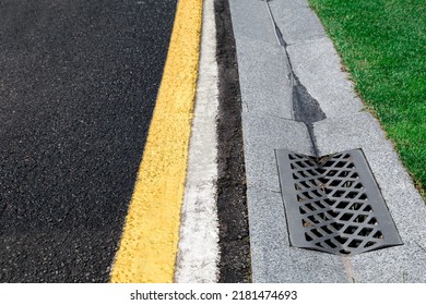 Gutter Of A Stormwater Drainage System On The Side Of An Road With Yellow And White Markings And Green Lawn On Wet Weather After Rain, Close Up View, Nobody.