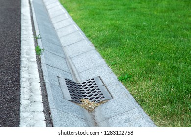 gutter of a stormwater drainage system in perspective on the side of an road with markings and lawn.
