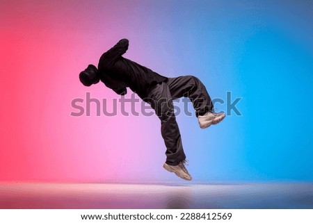 guy acrobat doing back fat in new lighting, male dancer jumps and falls in the air on red blue background, hiphop performer does trick and levitates in the air