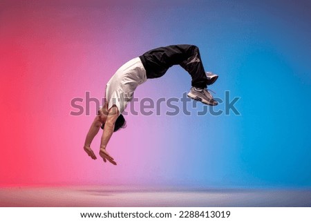 guy acrobat doing back fat in new lighting, male dancer jumps and falls in the air on red blue background, hiphop performer does trick and levitates in the air