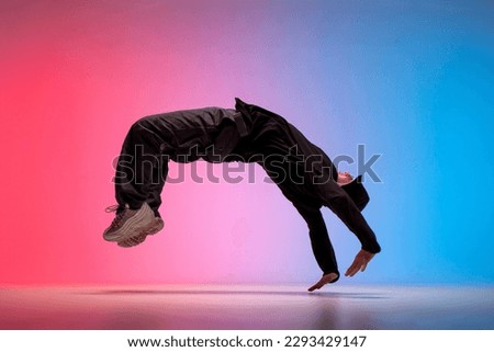 guy acrobat doing back fat in new lighting, male dancer jumps and falls in the air on red blue background, hiphop performer does trick and levitates in the air