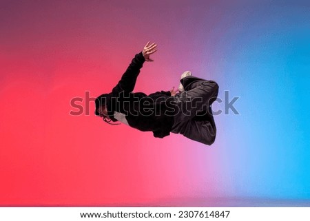 guy acrobat doing back fat in new lighting, male dancer jumps and falls in the air on red blue background, hiphop performer does trick and levitates in the air