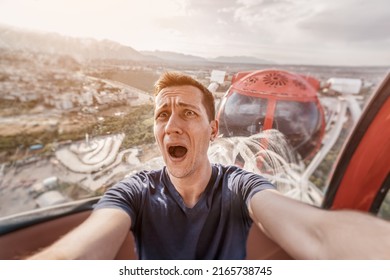 A guy with acrophobia or fear of heights screams with funny emotions on his face from the view from a high Ferris wheel in an amusement park