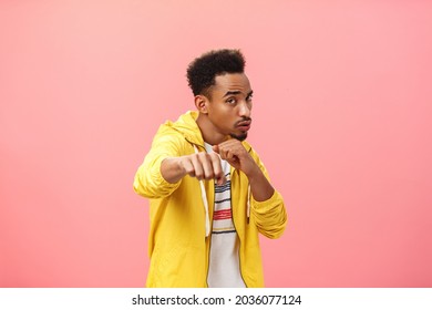 Guy acting cool bragging in front of girlfriend with mascules showing boxer moves standing in boxing pose with raised fist in punch gesture turning right as if fighting over pink background