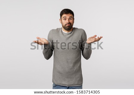 Guy asking help dont know what do. Perplexed, confused and indecisive cute clumsy bearded man in grey sweater, raise hands sideways, shrugging clueless, cant help, cannot answer, smirk saying sorry