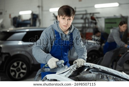 Guy auto mechanic performs car body work in auto repair shop. Auto mechanic young woman polishes vehicle body parts and restores attractive appearance of car, performs minor repairs.