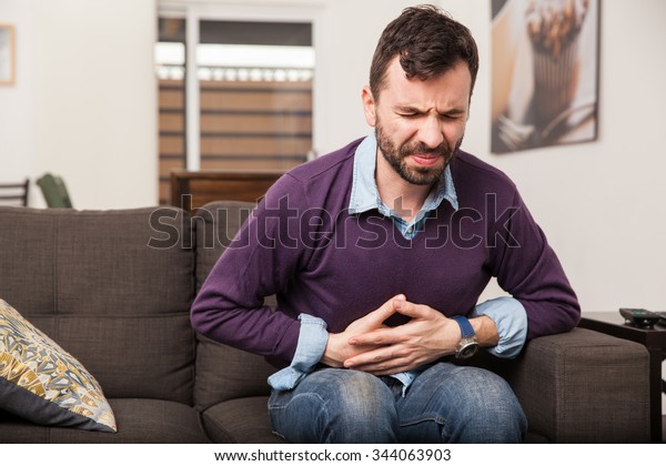 Guy with a beard feeling unwell with a\
stomach ache while sitting in a couch at\
home